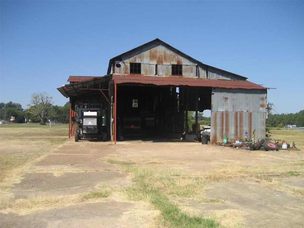 Weathered metal barn with open bays, a covered equipment shelter, and farm machinery on a dry rural property