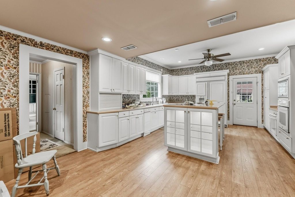 Spacious kitchen with white cabinetry, center island, hardwood floors, ceiling fan, and floral wallpaper accents