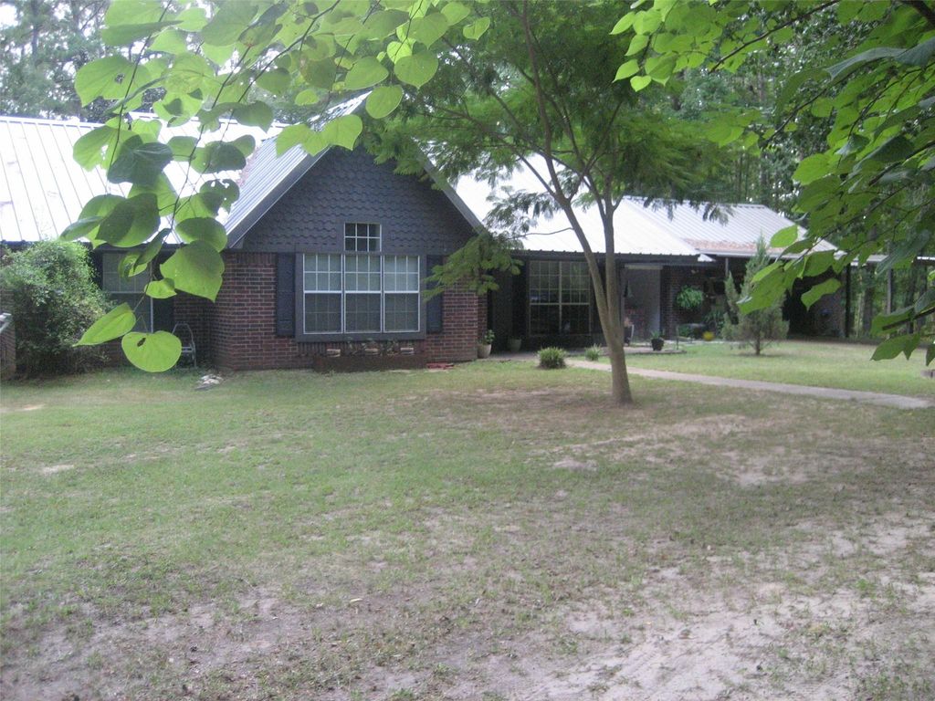 Brick ranch-style home with metal roof, dark shutters, and large front yard surrounded by trees