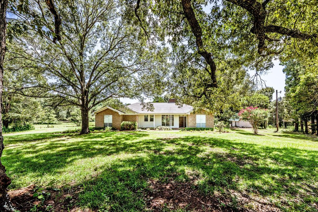 Single-story brick ranch home surrounded by large mature trees and a lush green lawn