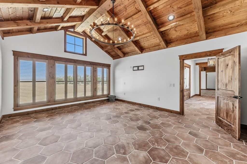 Spacious room with vaulted wood beam ceiling, hexagonal tile floor, plantation shutters, and a wrought iron chandelier