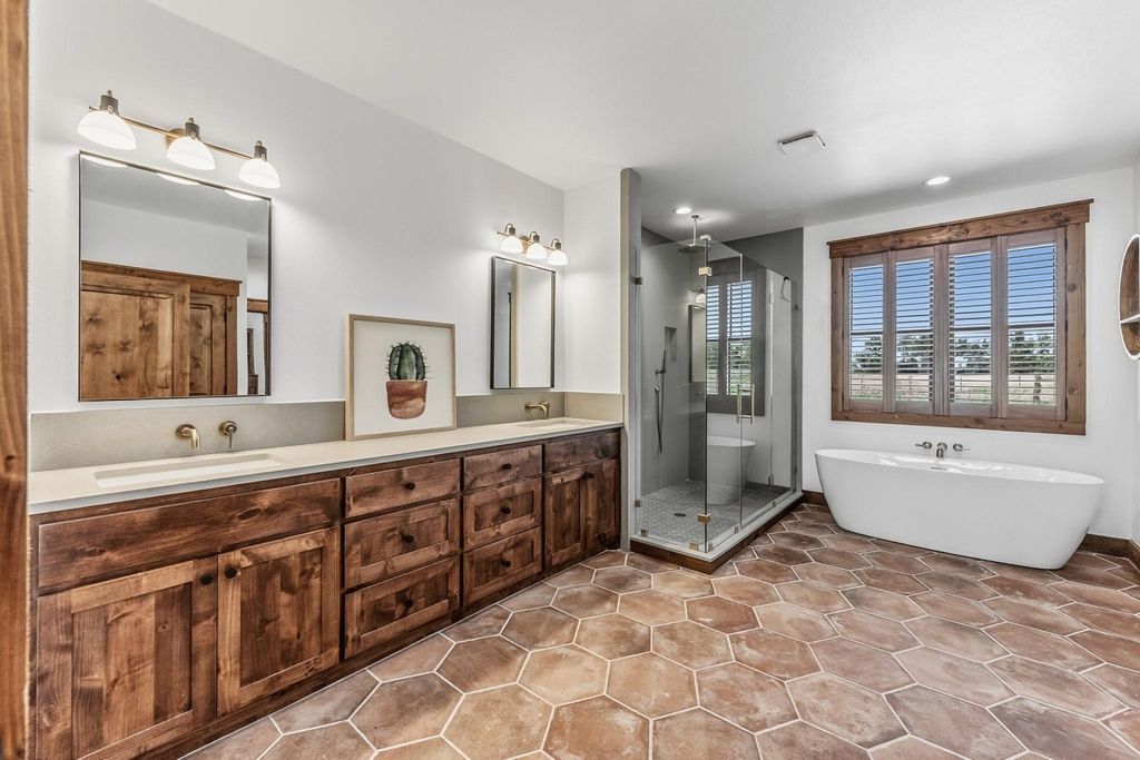 Spacious primary bathroom with double wood vanity, freestanding soaking tub, glass walk-in shower, and hexagonal tile floors